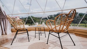 A room with a large glass dome, wicker chairs, a small table, and a view of a green landscape. - Vida Aventura Ranch (Mogote de Bagaces)