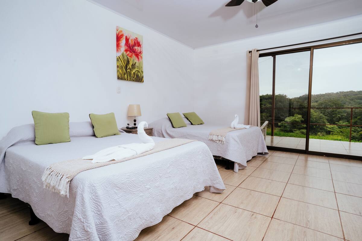A hotel room with two beds, a large window, and a painting on the wall.