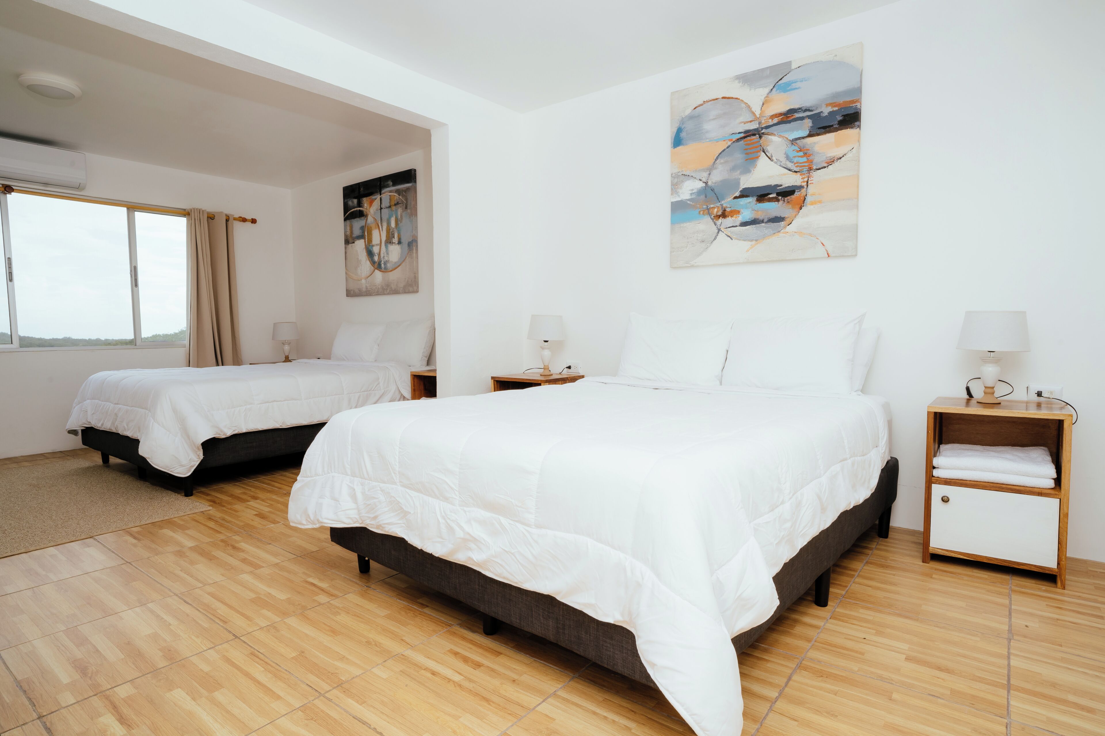 A hotel room with two beds, a large abstract painting, a window, and a wooden floor.