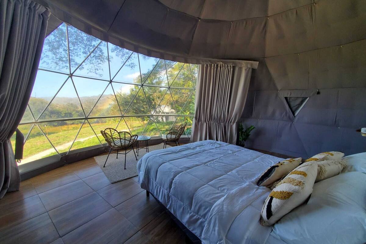 A bedroom with a large window, a bed, and a small table with chairs.