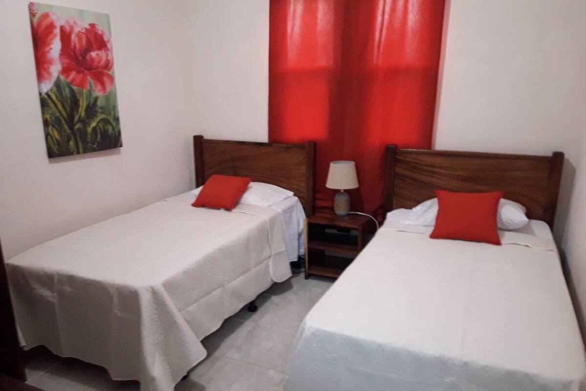A hotel room with two single beds, a nightstand with a lamp, and a painting on the wall.