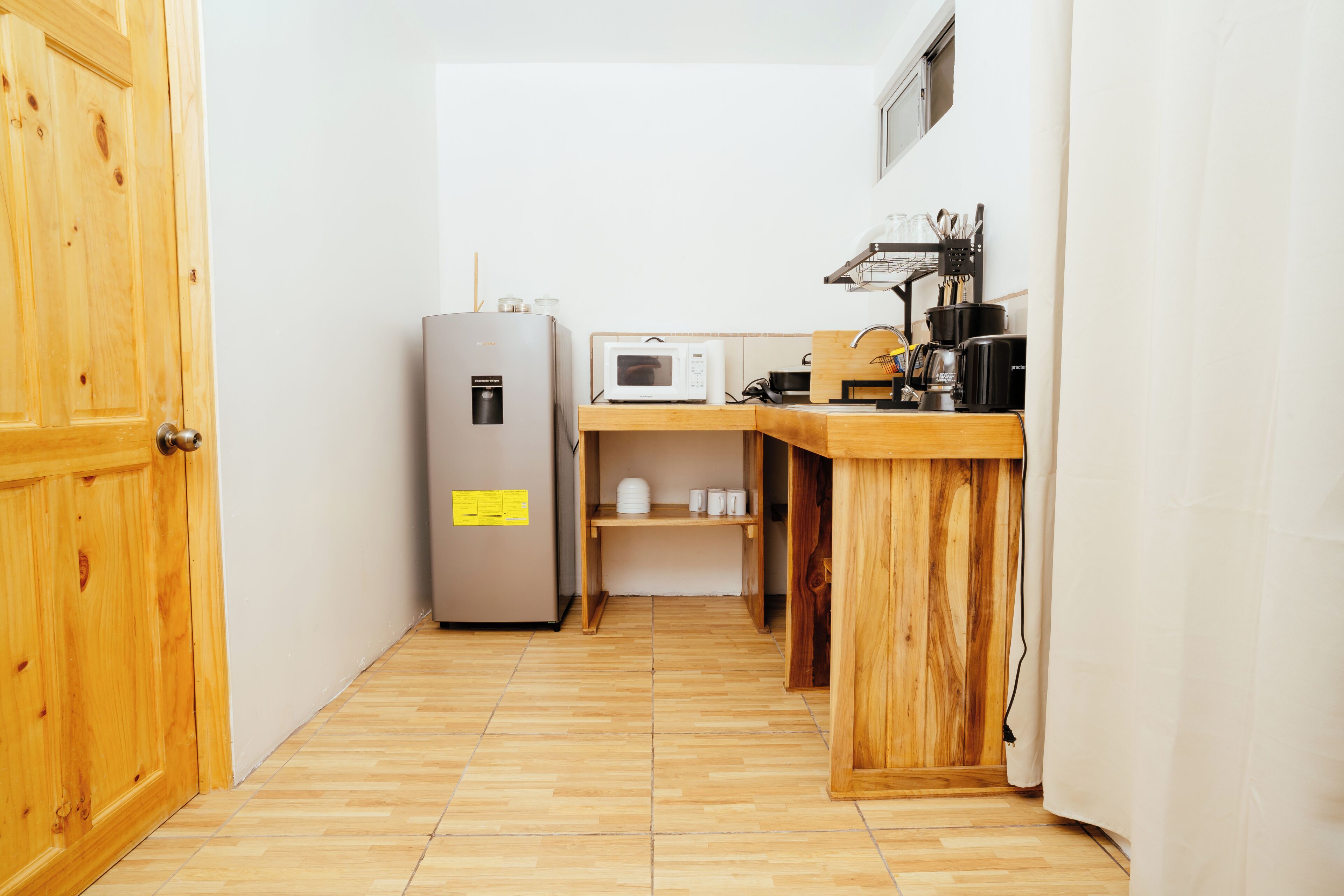 Cozinha compacta com geladeira, micro-ondas e bancada de madeira.