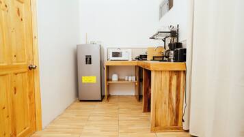 Cozinha compacta com geladeira, micro-ondas e bancada de madeira.