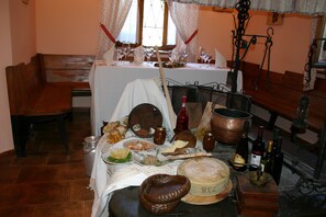 A dining table set with various food items, bottles, and a large cheese wheel. - Albergo Alle Alpi (Comeglians)