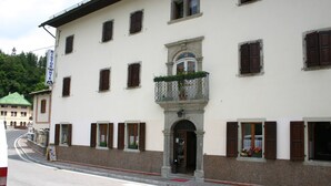 A white building with multiple windows and a balcony with potted plants. - Albergo Alle Alpi (Comeglians)