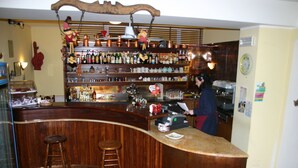A bar area with wooden bar counter, stools, and shelves stocked with bottles and glasses. - Albergo Alle Alpi (Comeglians)