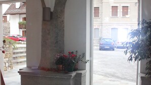 A stone-floored corridor with an arched doorway leading outside. There are potted plants and a bench along the corridor. - Albergo Alle Alpi (Comeglians)