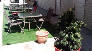 Un patio al aire libre con una mesa, sillas, una planta en maceta y un edificio con puertas numeradas 5 y 6.
