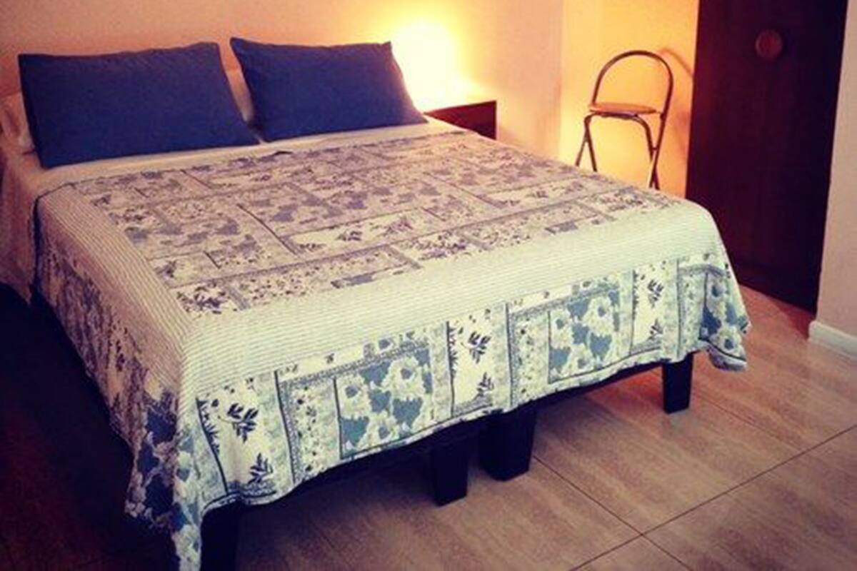 A bed with a patterned bedspread, two pillows, a nightstand with a lamp, and a door to the right.