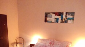 Una cama bien hecha con un edredón estampado, una pequeña silla y un cuadro abstracto colgado en la pared.