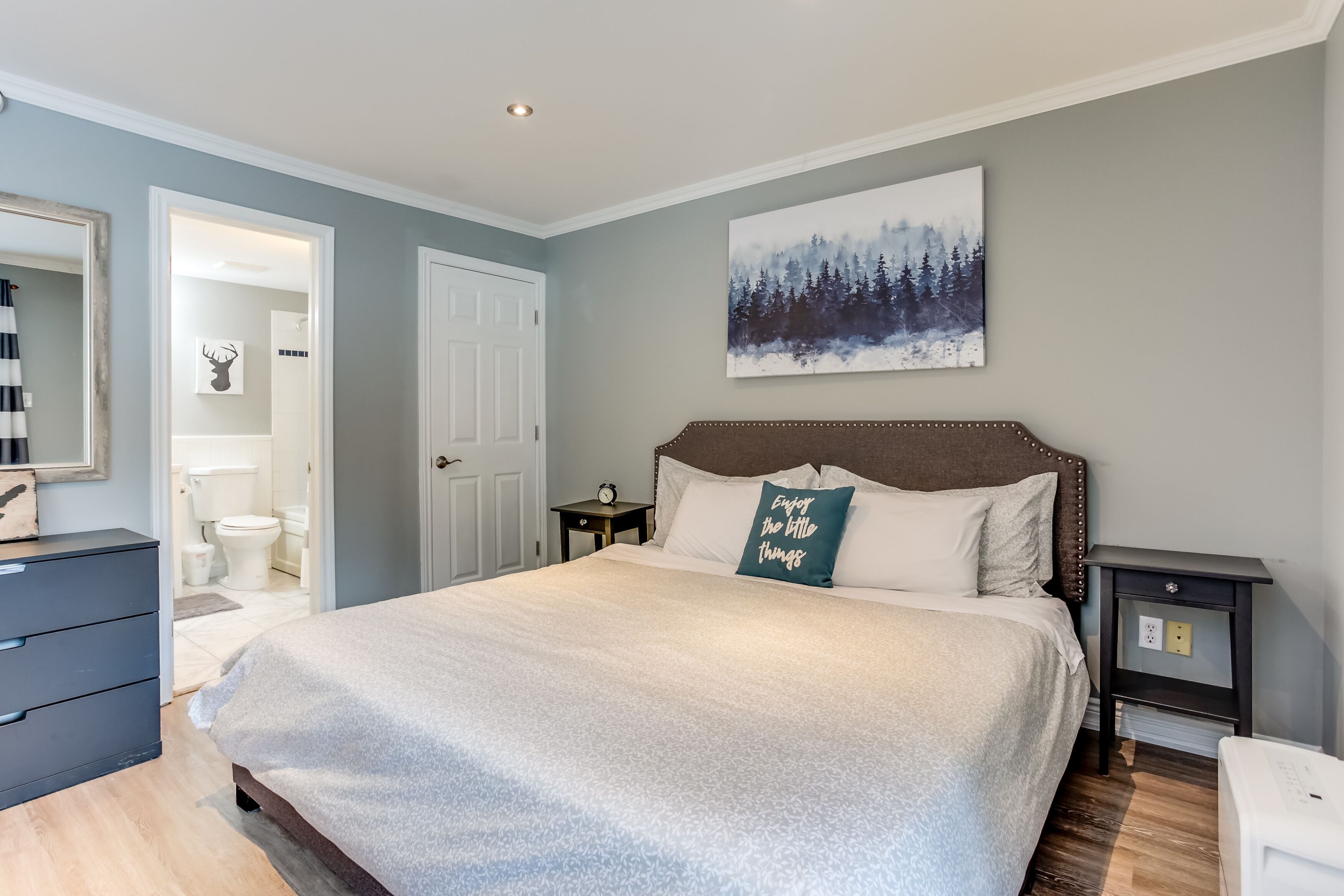 A bedroom with a large bed, a nightstand, a dresser, and a painting on the wall.
