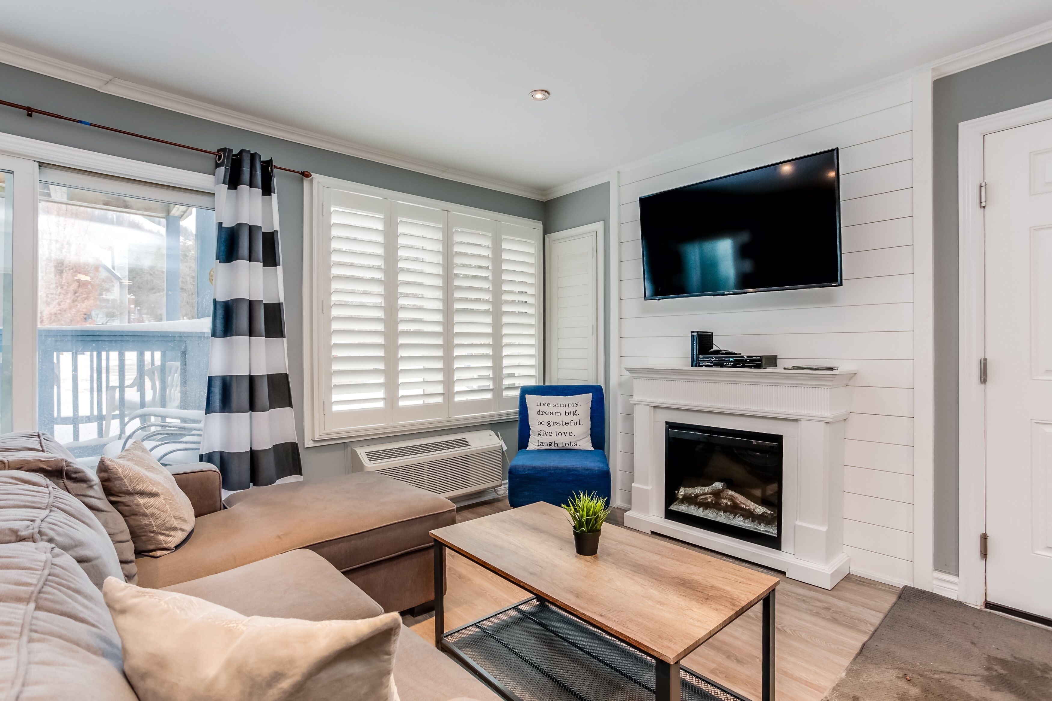 A living room with a sofa, a coffee table, a fireplace, a TV, and a window with blinds.