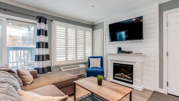 A living room with a sofa, a coffee table, a fireplace, a TV, and a window with blinds.