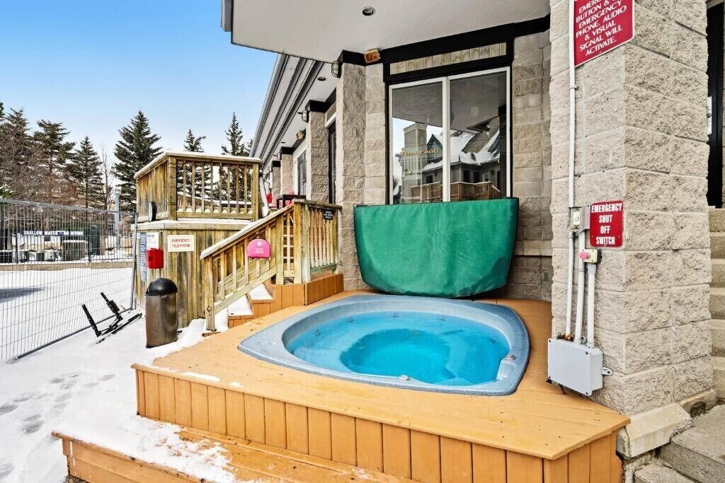 Ein hölzernes Whirlpool vor einem Steinhaus, mit Telefon und Not-Aus-Schalter.