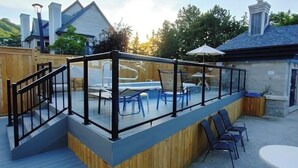 Una terraza con barandilla de cristal, piscina y zona de estar exterior.