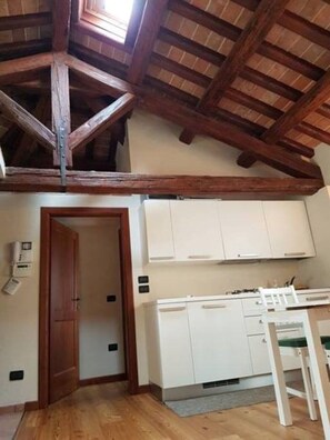 Cozinha com armários brancos, teto de madeira e porta que dá para outro cômodo.