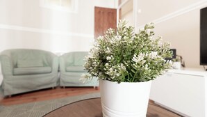 Una planta blanca en maceta sobre una mesa redonda en un salón con dos sillones verdes y suelo de madera.