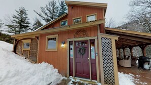 A wooden cabin with a red door, a covered porch, and a snow-covered deck. - Ledges by GetAway (Bridgewater Corners)