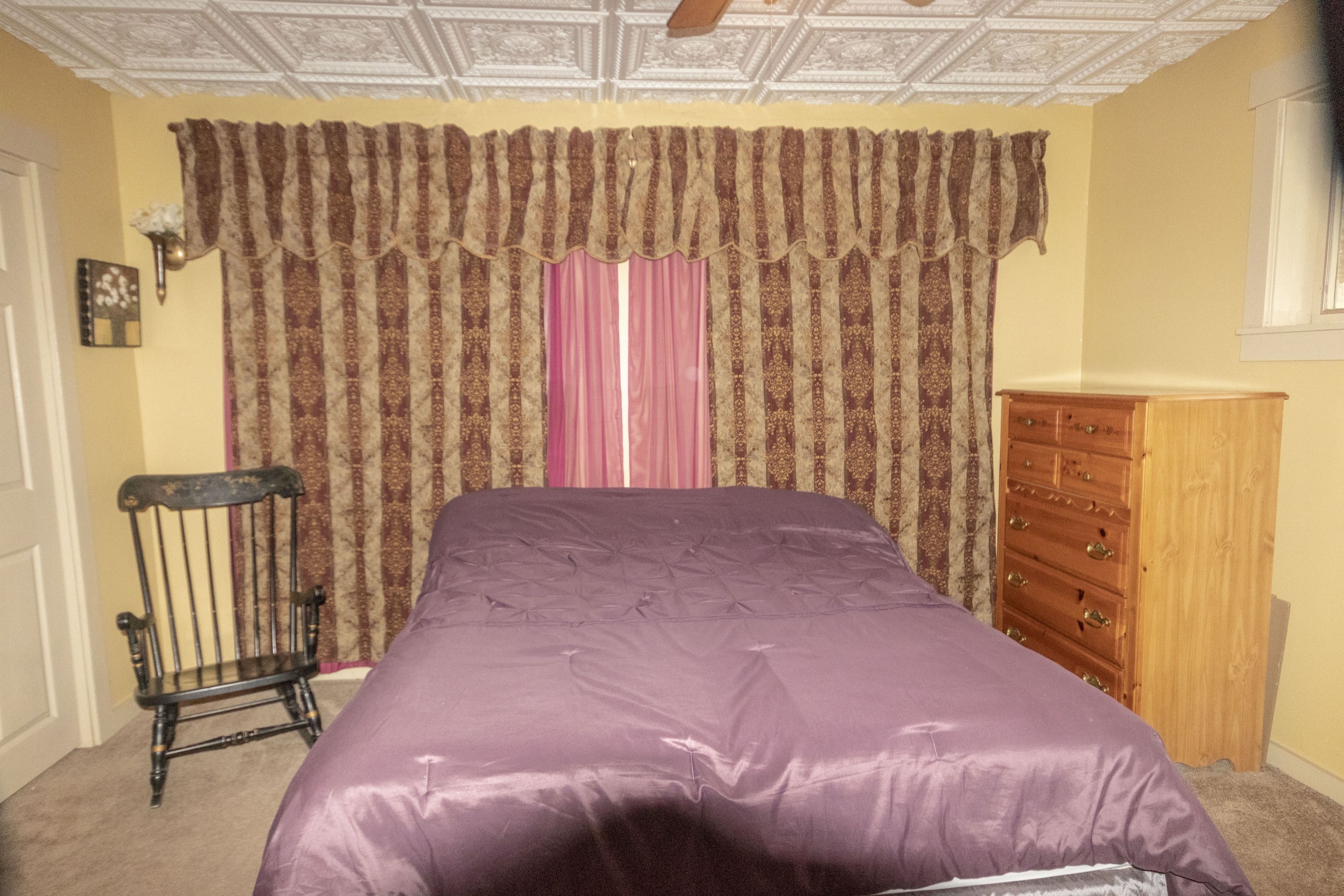 Un dormitorio con una cama, un aparador de madera, una silla y una cortina estampada.