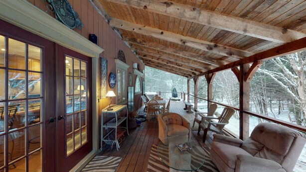 A covered porch with wooden beams, a seating area with chairs and a table, and a view of snow-covered trees. - Ledges by GetAway (Bridgewater Corners)
