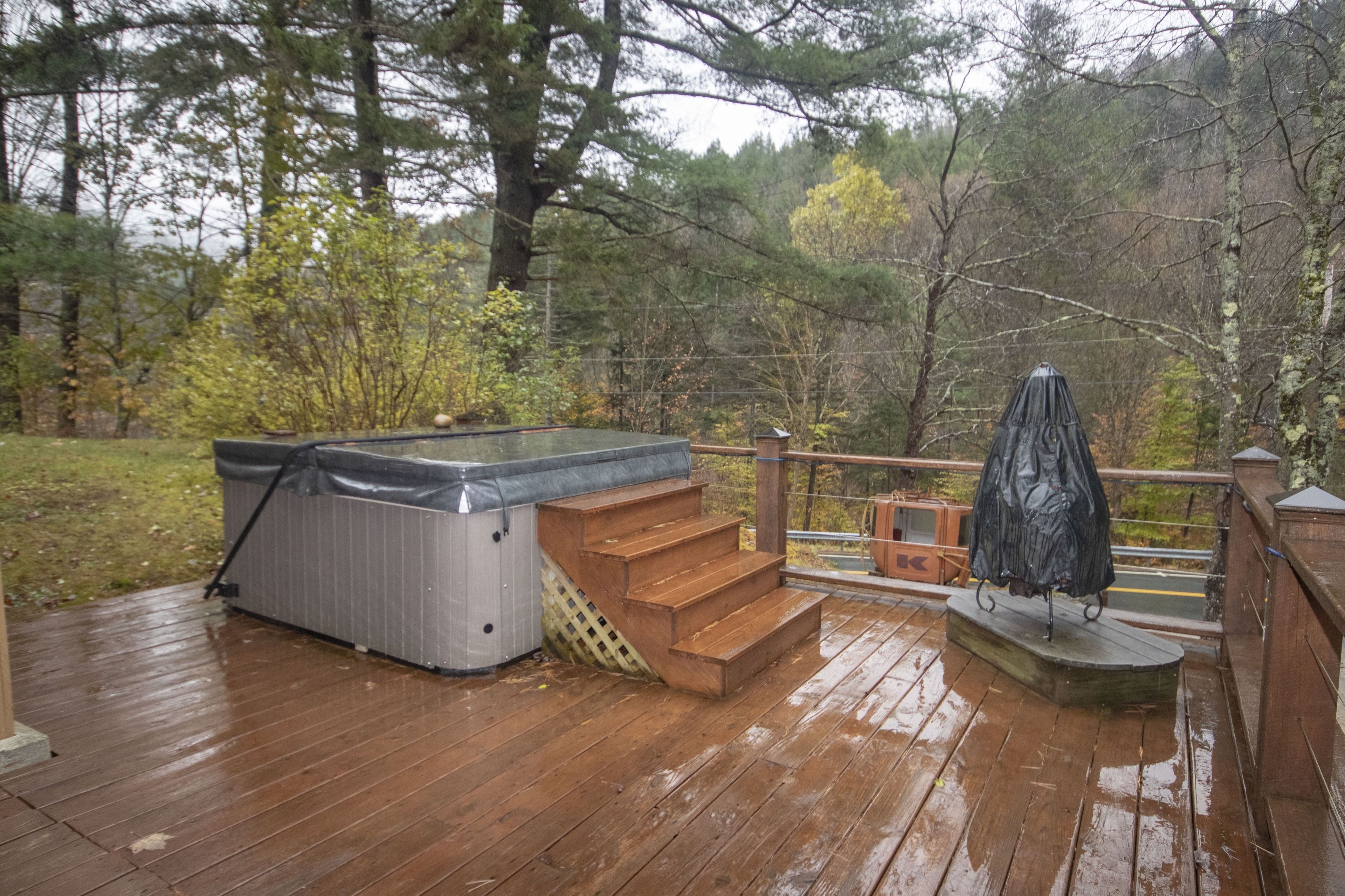 Una terraza de madera con un jacuzzi, escaleras y una sombrilla.