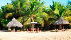 Ein Strand mit Strohdächern, Holztischen und -stühlen.