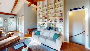 Ein gemütliches Wohnzimmer mit einem weißen Sofa, einem Bücherregal voller Bücher und Dekorationen sowie einer Holztreppe.
