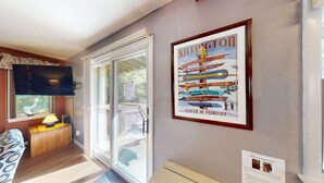 Ein Zimmer mit großem Fenster, einem gerahmten Poster an der Wand, einem flachbildschirmfernseher über einem Holztisch und einem kleinen Tisch mit Lampe.