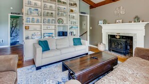 Ein Wohnzimmer mit einem weißen Sofa, einem Couchtisch und einem Kamin. Regale mit verschiedenen Gegenständen und eine Treppe, die in einen anderen Raum führen.