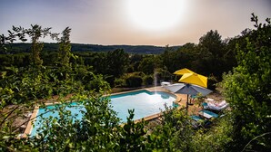 Une piscine entourée de chaises longues et de parasols, avec une végétation luxuriante et des collines en arrière-plan.