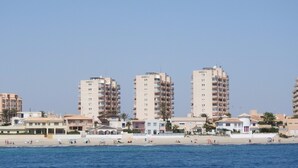 A coastal cityscape with high-rise buildings, a sandy beach, and clear skies.