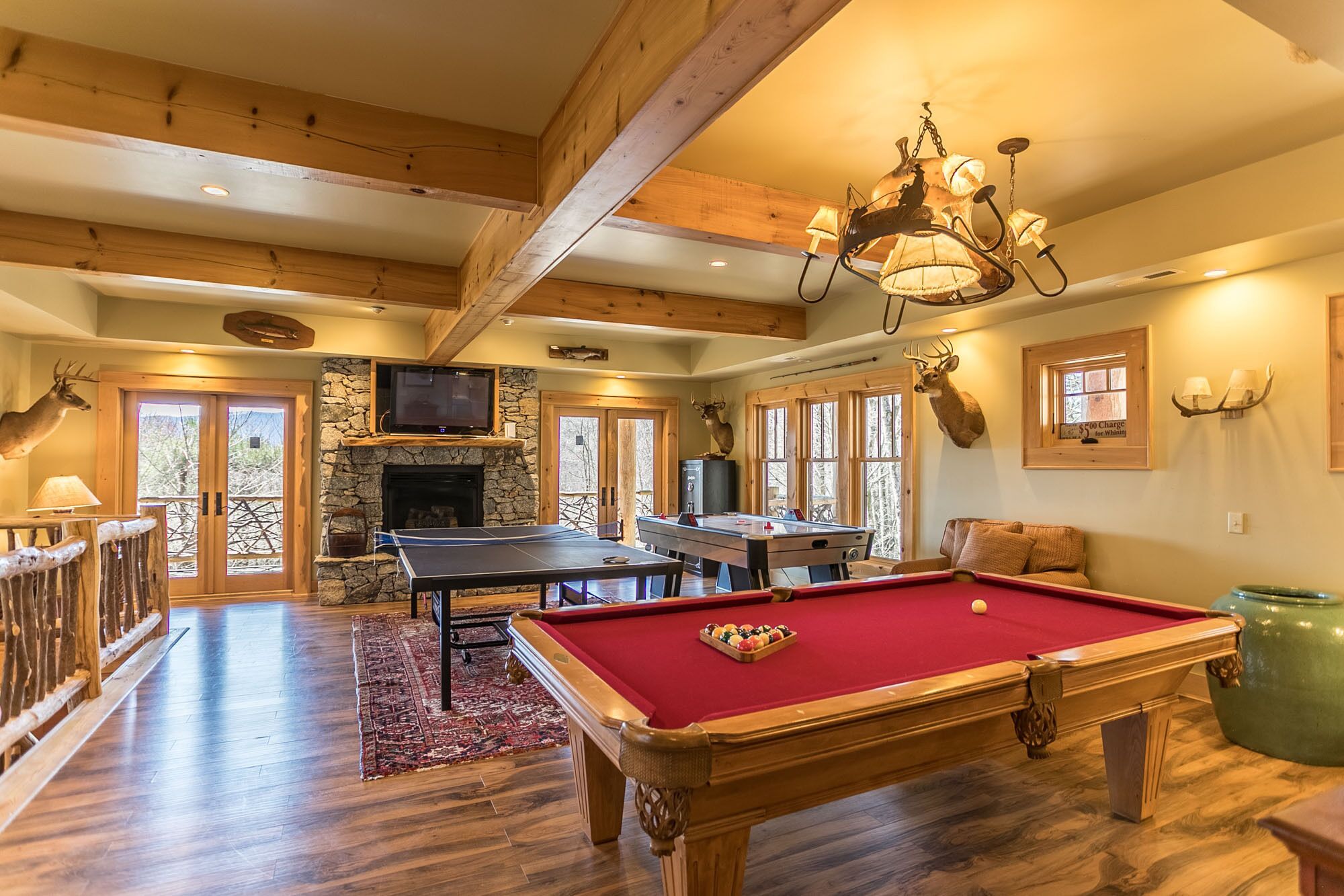 A spacious room with a pool table, a fireplace, and a television mounted on a stone wall.