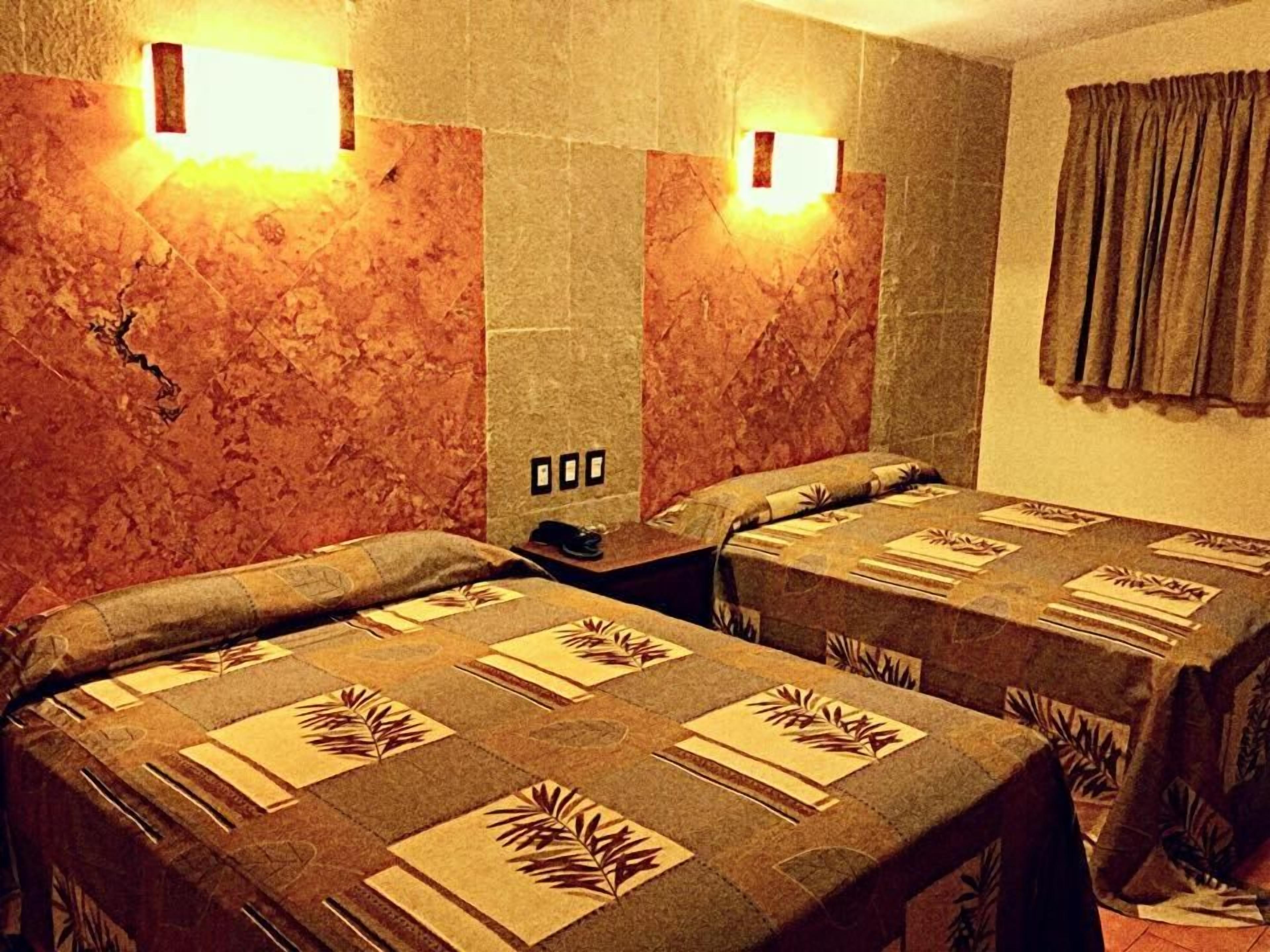 Una habitación de hotel con dos camas, una mesita de noche, un teléfono y una cortina.