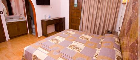 Un dormitorio con cama, escritorio, lavamanos y puerta.