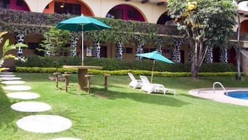 Un patio con piscina, sillas de descanso y una mesa con sombrillas.