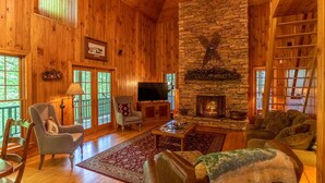 Un acogedor interior de cabaña de madera con chimenea de piedra, paredes de madera y un televisor.