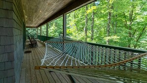 Una hamaca en una terraza de madera con vistas a un bosque.
