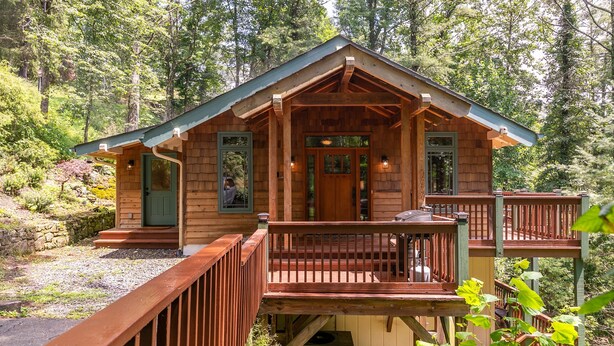 Une cabane en bois dotée d’un porche et d’une terrasse, entourée d’arbres.