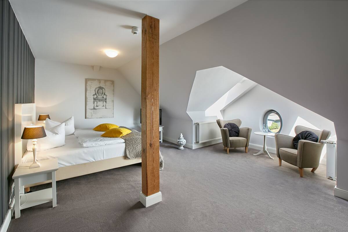 A modern bedroom with a large bed, a sitting area with two chairs, a small table, and a large window.