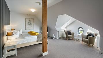 A modern bedroom with a large bed, a sitting area with two chairs, a small table, and a large window.