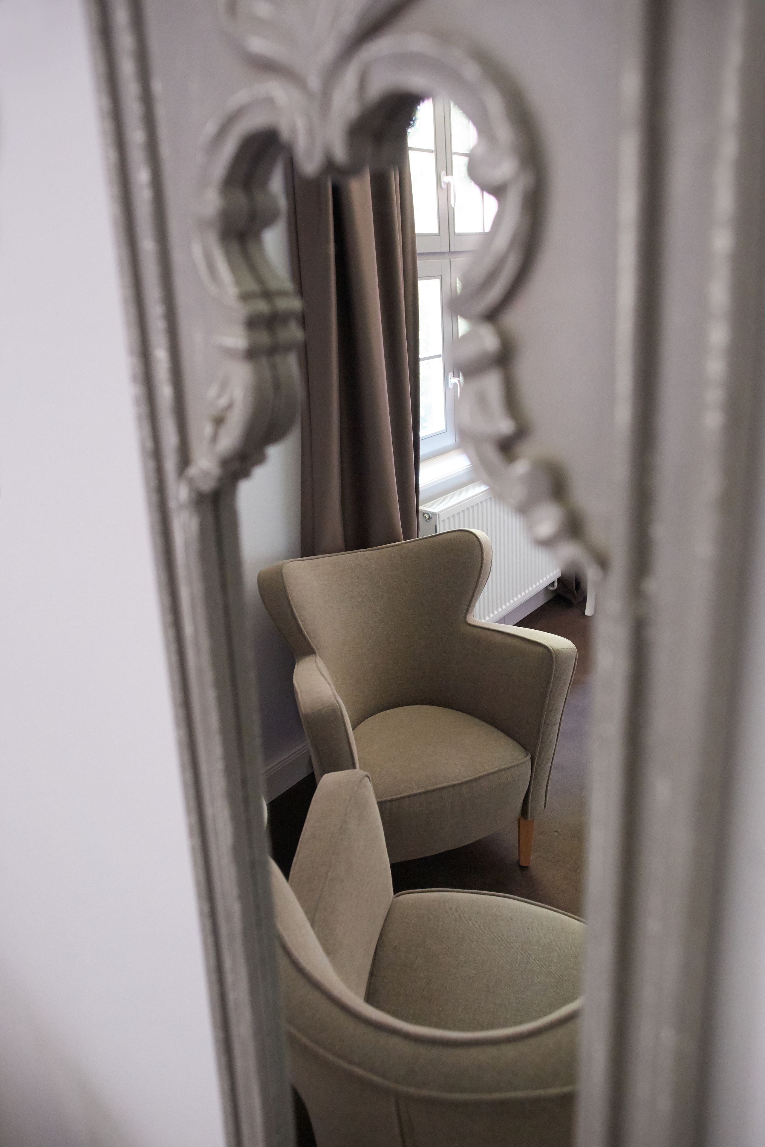 Une pièce avec une chaise et un miroir qui reflète une fenêtre et des rideaux.