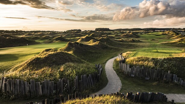 Un campo de golf con un camino serpenteante y vallas de madera.