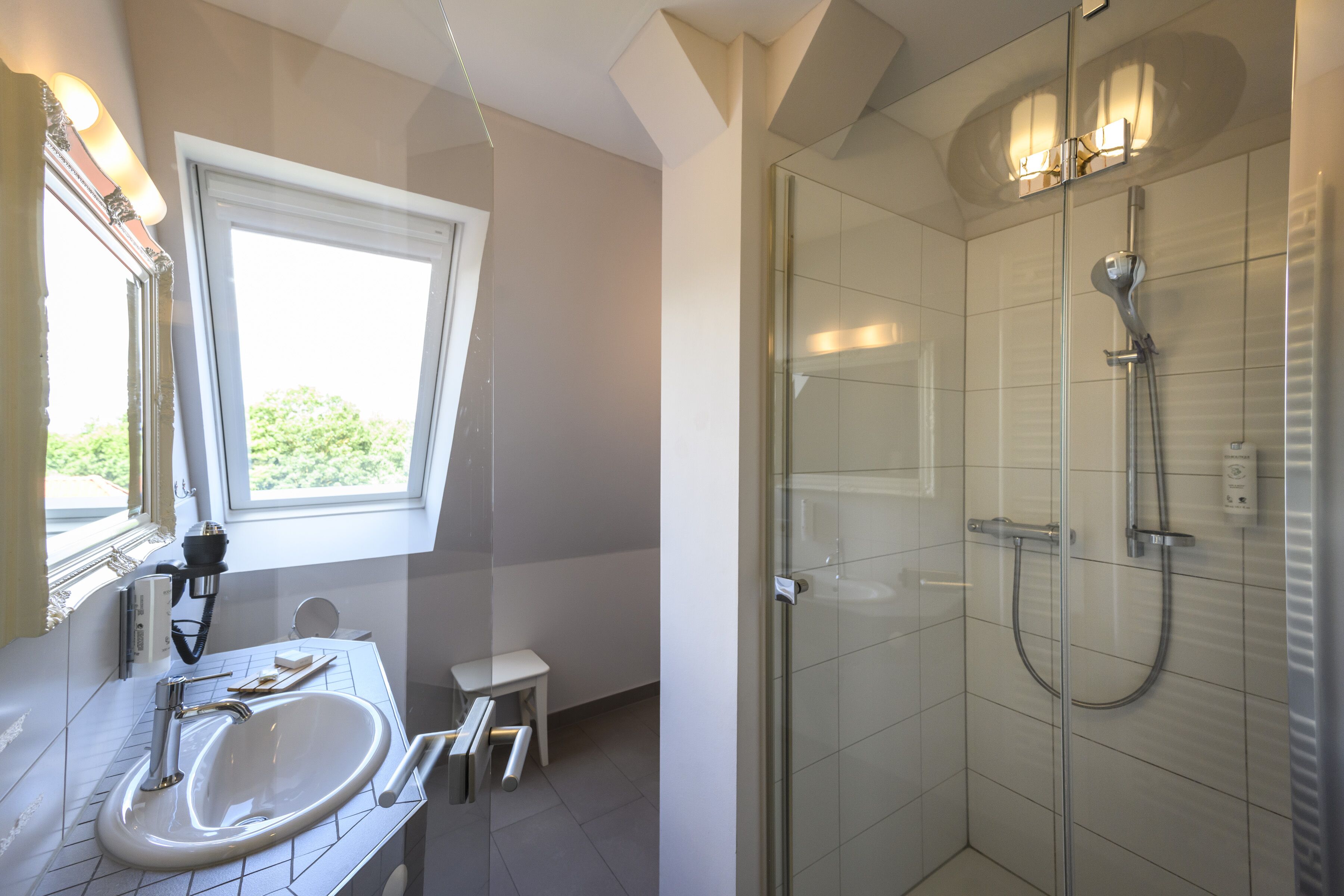 Un baño moderno con un lavamanos grande, un taburete pequeño y una zona de ducha con mampara de vidrio.