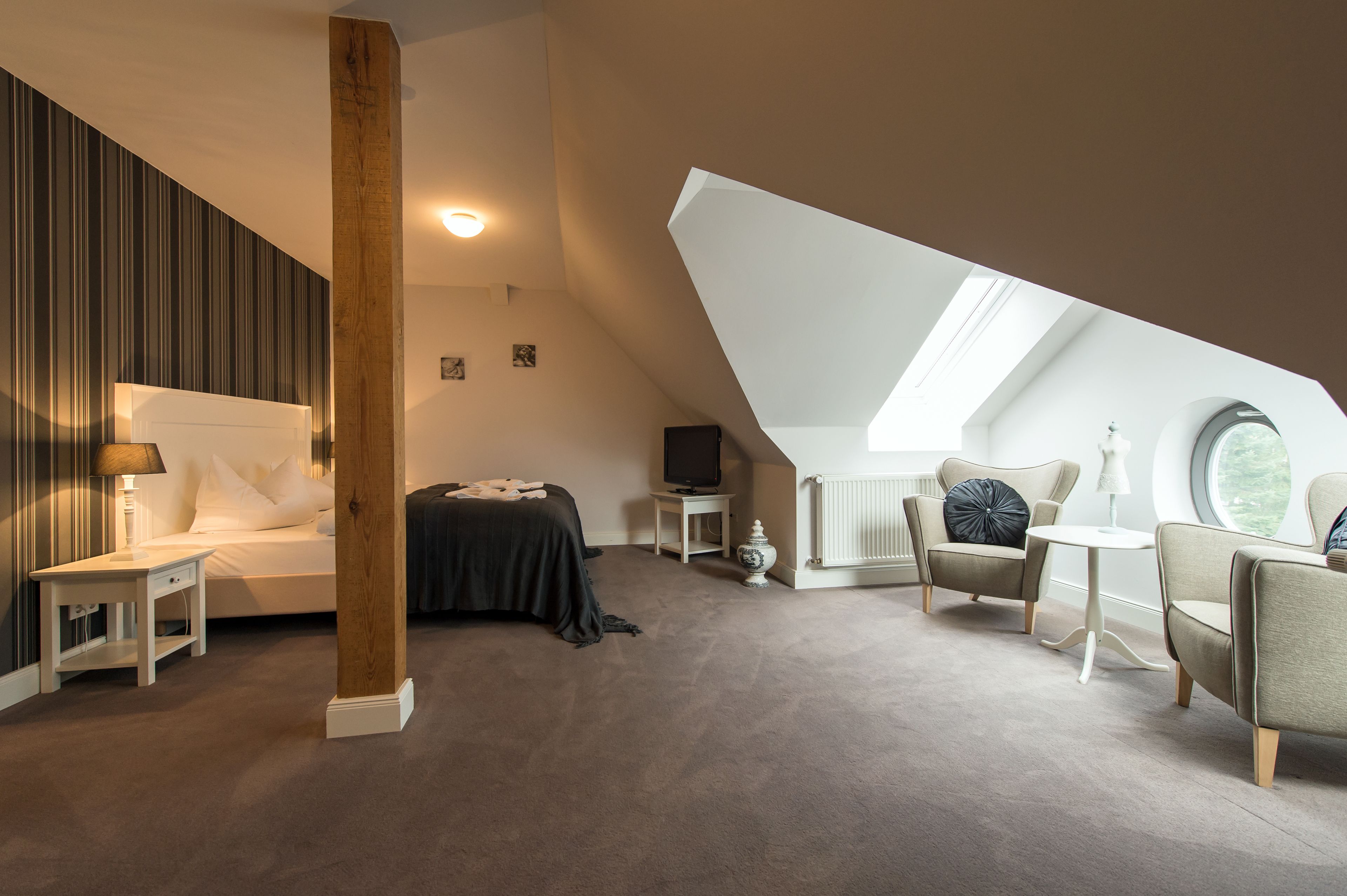 A bedroom with a sloped ceiling, a bed, a TV, a chair, and a small table.