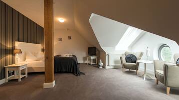 A bedroom with a sloped ceiling, a bed, a TV, a chair, and a small table.
