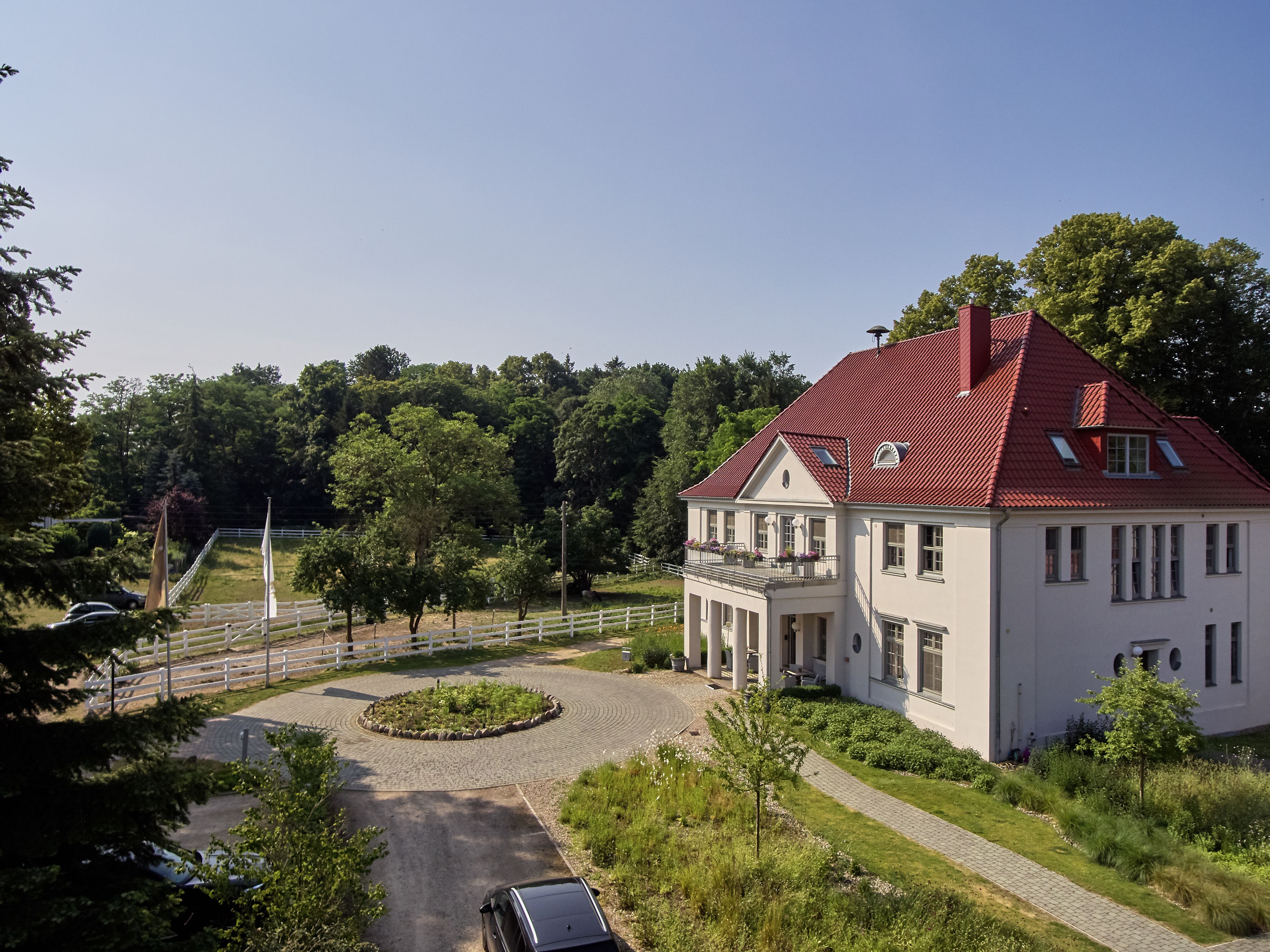 A large, white building with a red roof, surrounded by lush greenery and a paved driveway.