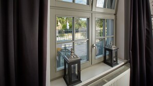 Una ventana con dos faroles negros en el alféizar, un radiador blanco debajo, y vistas a un patio exterior con mesas y sillas.