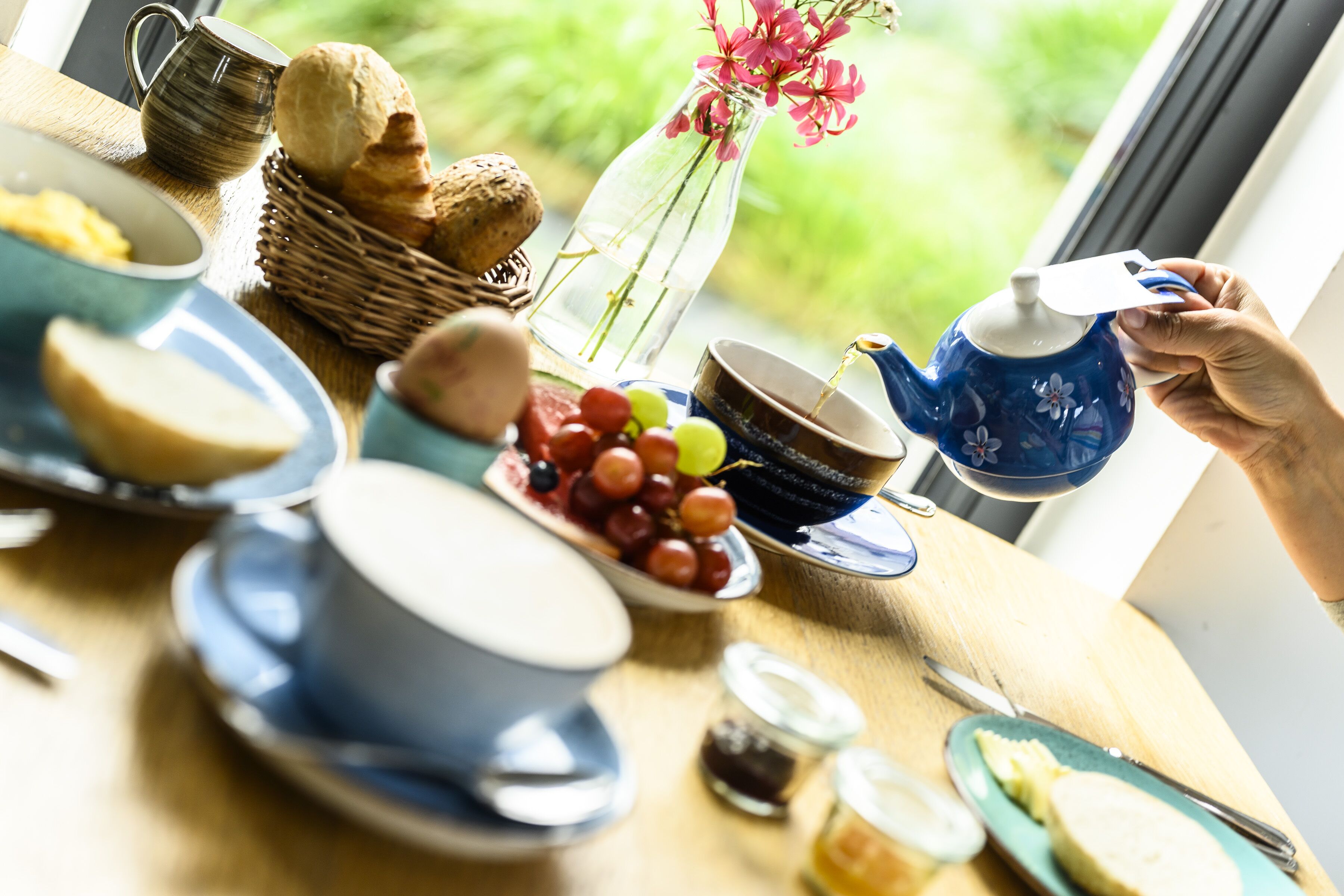 Een ontbijttafel met borden, een theepot en uitzicht uit het raam.