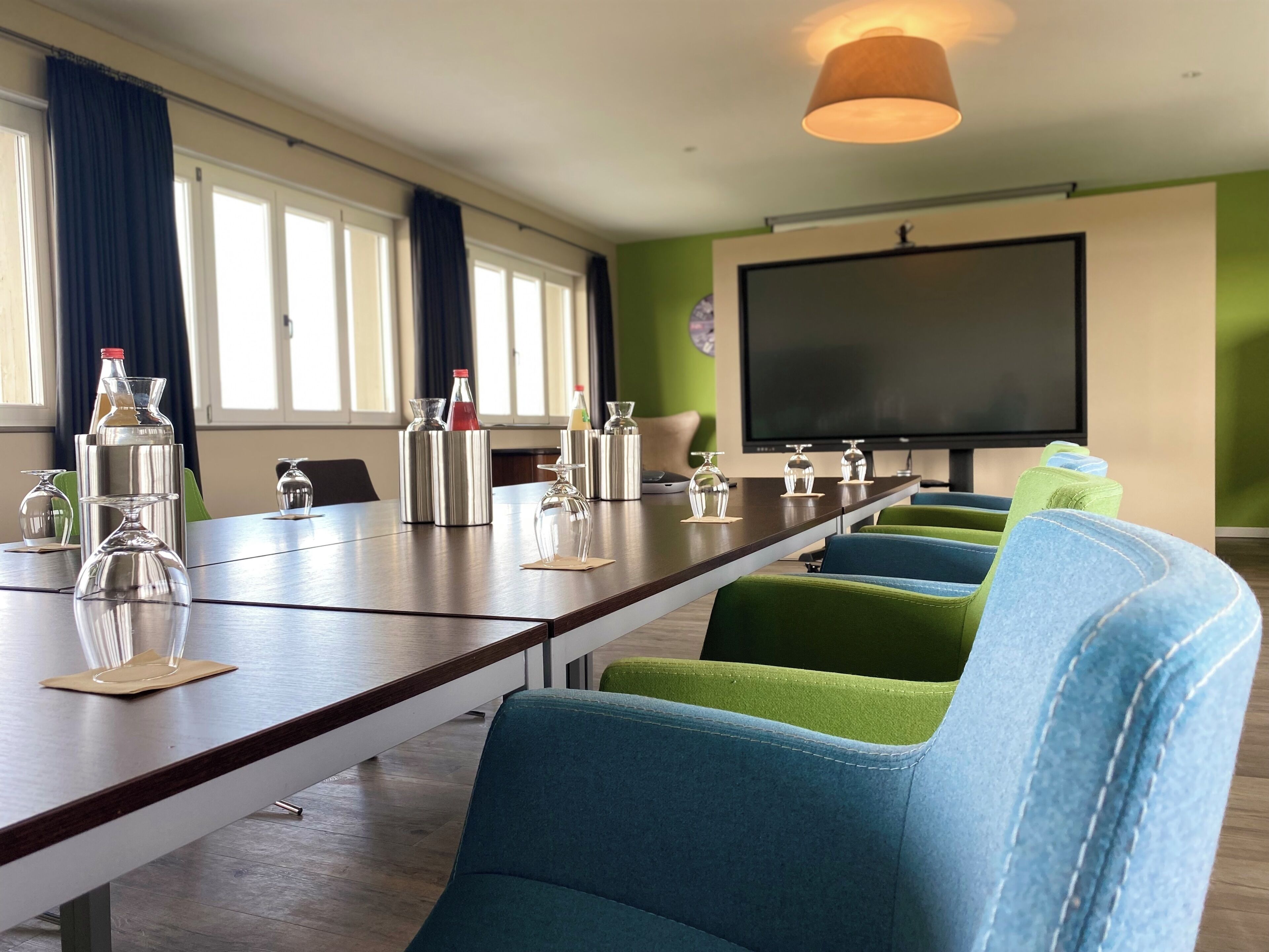 Un salón de conferencias con una larga mesa, sillas, una pantalla de proyector y varios vasos.