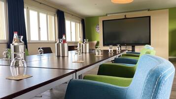 Un salón de conferencias con una larga mesa, sillas, una pantalla de proyector y varios vasos.